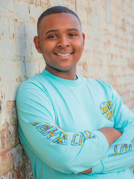 Young African American man in a blue standing against a white brick wall in a senior photo