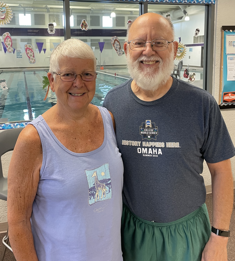 Older woman in a purple tank top standing next to an older man in a dark gray shirt. Both are smiling.